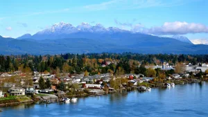 Fraser River waterfront homes and boats in Maple Ridge with snow-dusted mountains and blue skies.