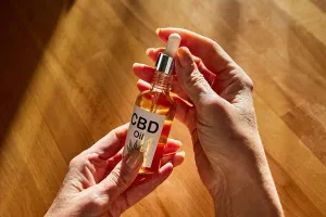 Hands holding a clear CBD oil tincture bottle against a wooden table