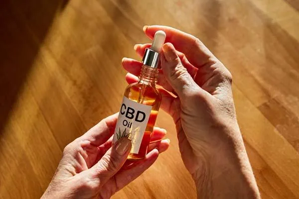 Hands holding a clear CBD oil tincture bottle against a wooden table