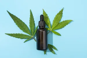 Amber CBD oil dropper bottle on blue background with cannabis leaves