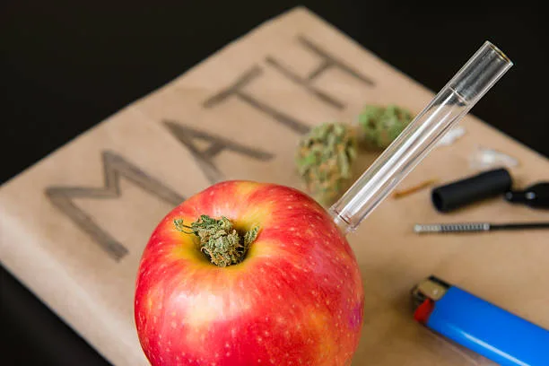A finished red apple pipe with cannabis flower packed in the top bowl and a glass mouthpiece inserted, sitting on a book.